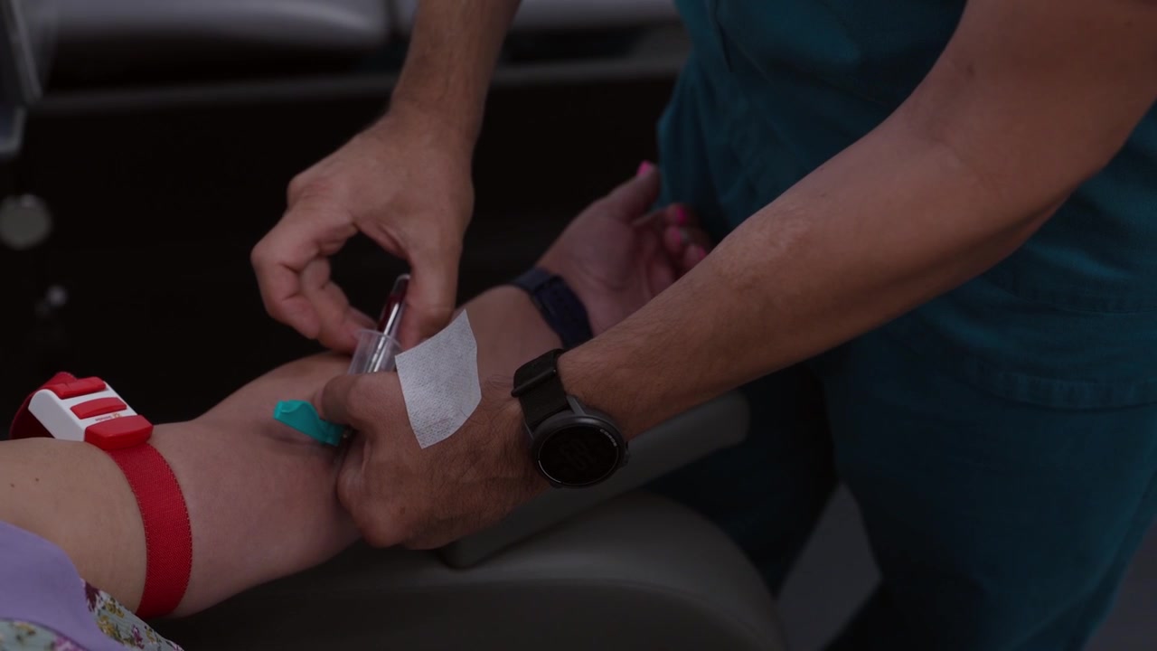 Primo piano di un professionista sanitario che esegue una procedura di venipuntura per prelevare un campione di sangue da un paziente utilizzando un laccio emostatico e una provetta sottovuoto.