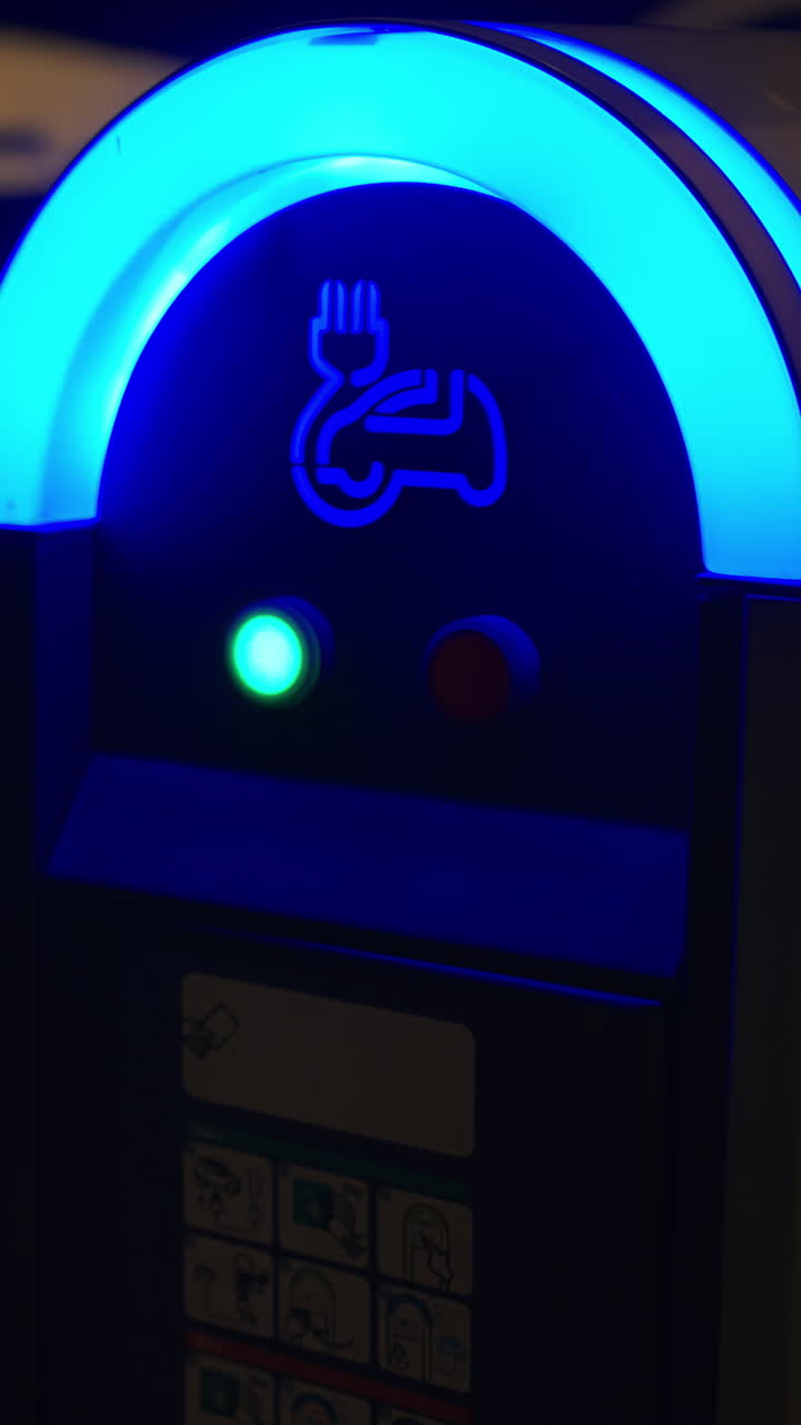 Close up of an illuminated, electric charging station at night. Vertical