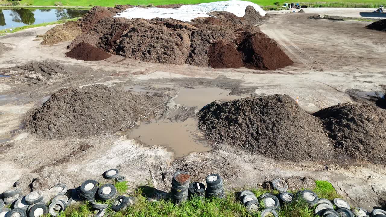 Aerial footage shows large mulch and soil piles surrounded by tires on a farm under bright daylight