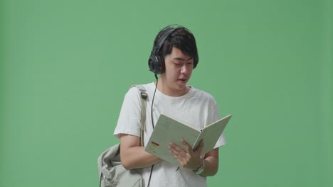 asian man student reading book and listening music with headphones on green screen studio