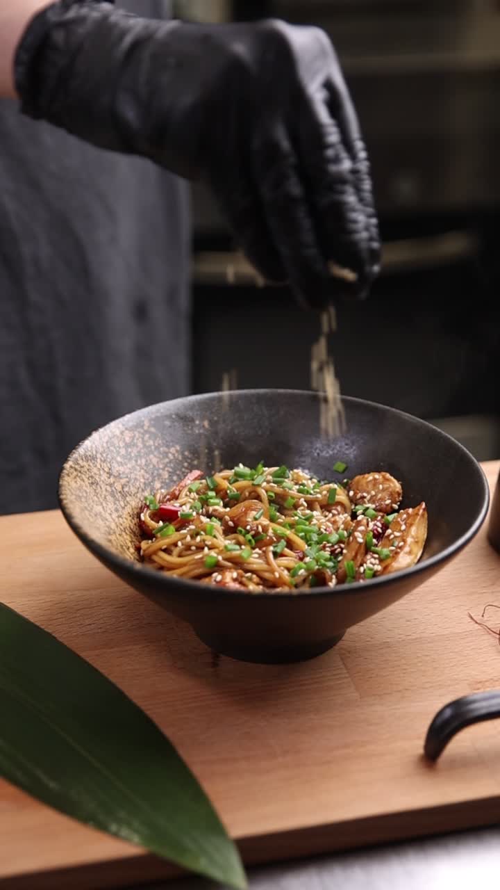 Chef che guarnisce noodles asiatici al wok con semi di sesamo