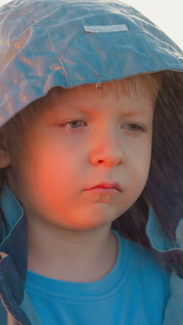 expresión de niño abandonado contra la puesta del sol. niño decepcionado empapado de lluvia y cansado se encuentra solo en la orilla del río. esperanza de encontrar seguridad lejos de casa