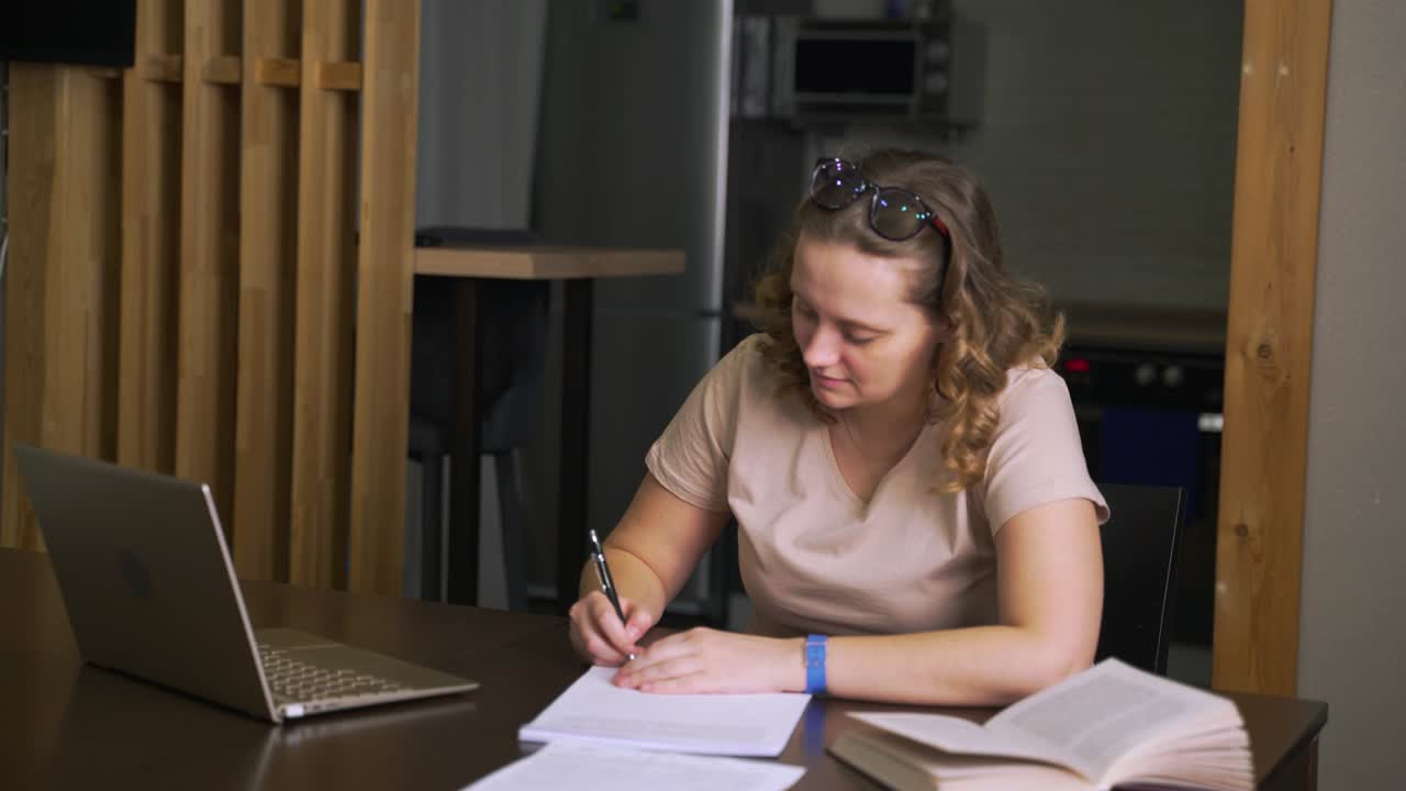 Woman signs papers for work or study. There is stack of contracts in front of her, she puts signature on sheet and puts it aside. Working at home, e-learning, pandemic, quarantine, distance