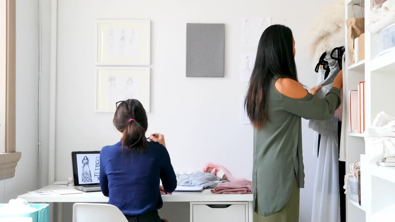 diseñador de moda trabajando en la computadora portátil y clasificando ropa en la percha 4k