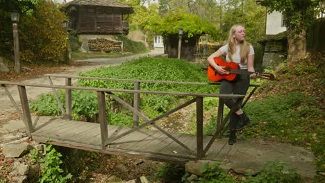 Beautiful-young-woman-strums-acoustic-guitar-rustic-wooden-bridge