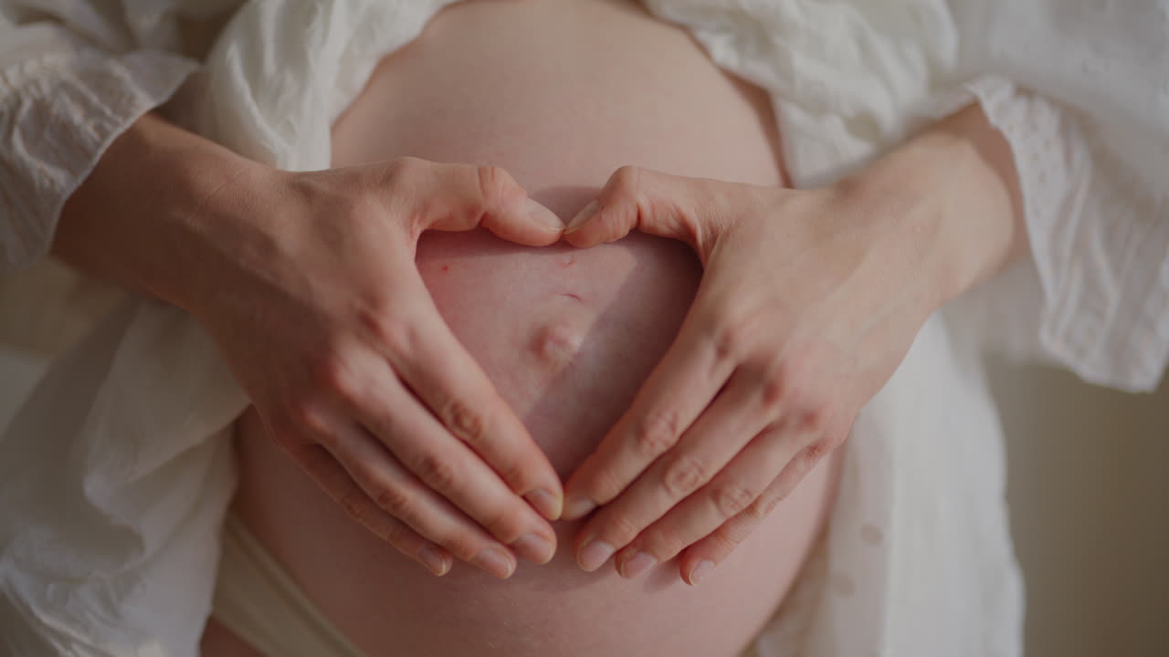 Donna incinta forma un cuore con le mani sulla pancia