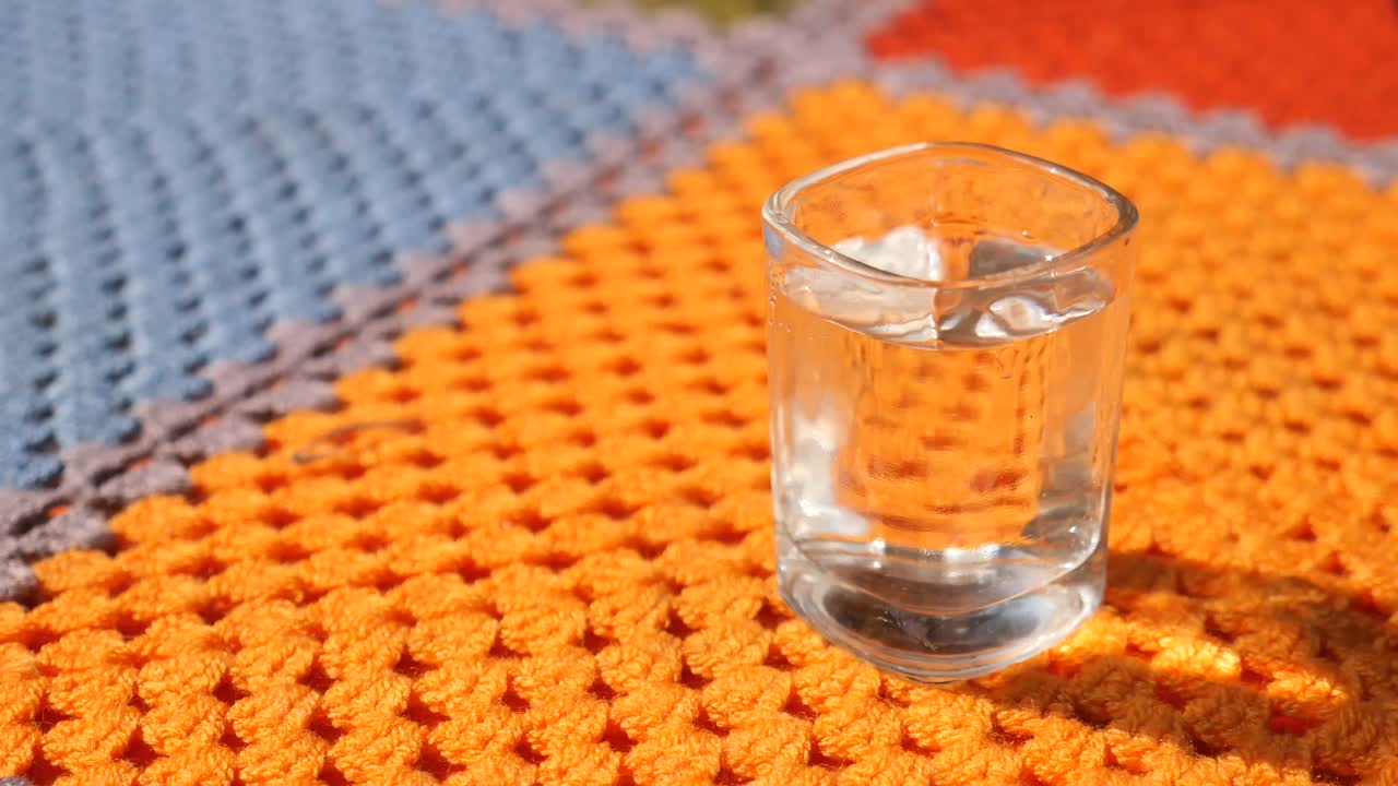 Vaso pequeño de líquido transparente sobre una manta de ganchillo