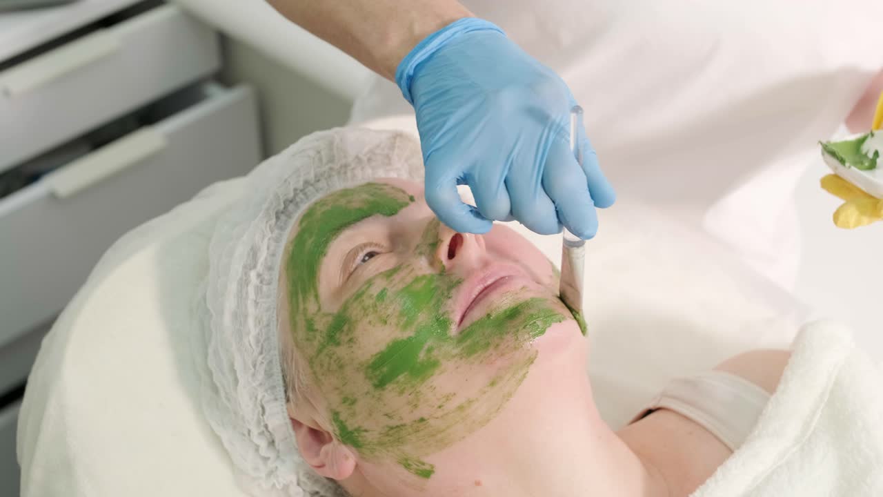 Profesjonelle ansiktspleieprosedyrer i en moderne kosmetologiklinikk. Påføring av ansiktsmaske.