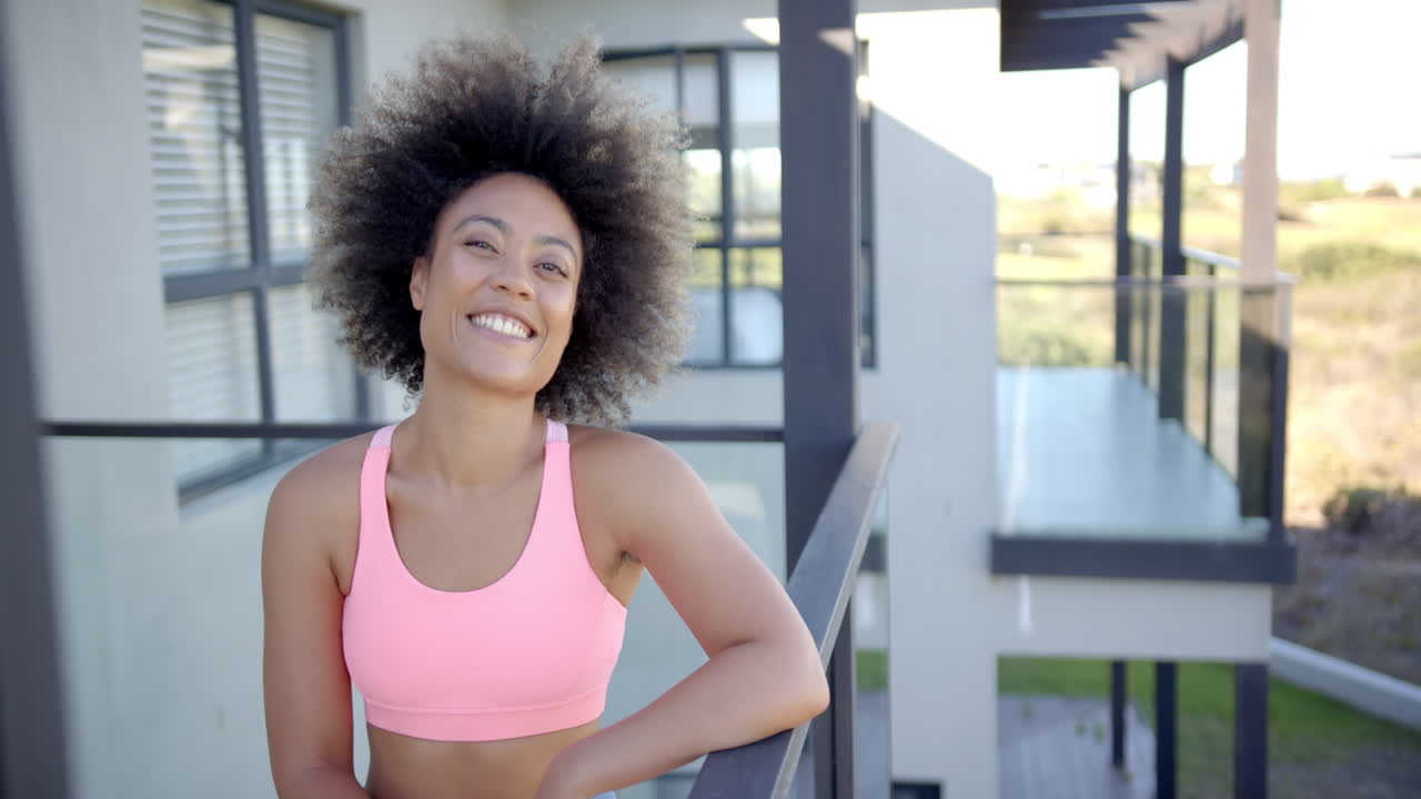 Smiling woman in sports bra standing on balcony, enjoying sunny day