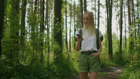 Una-Mujer-Atractiva-Se-Relaja-En-El-Bosque-Y-Usa-Un-Teléfono-Inteligente-Al-Aire-Libre.-Mujer-Caminando-Por-El-Bosque-Y-Escribiendo-Mensajes-En-Un-Teléfono-Inteligente.-Excursionista-Solitaria-Usando-Un-Teléfono-Inteligente.