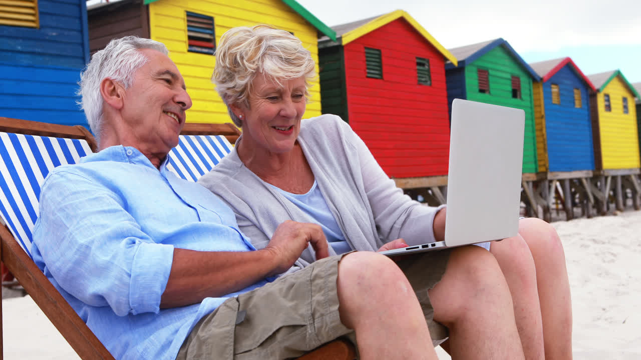 Senior couple using laptop at the beach