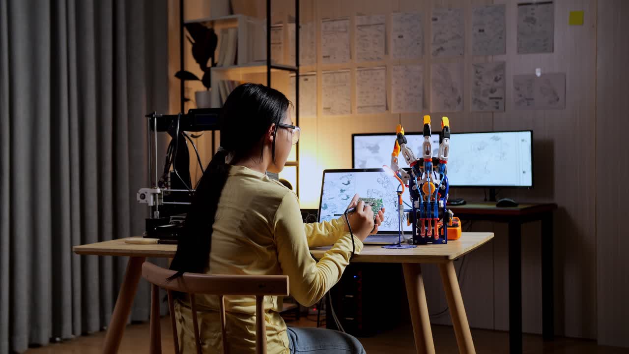 집에서 사이보그 손을 수리하는 동안 회로판을 들고 고치는 십대 아시아 소녀의 뒷면