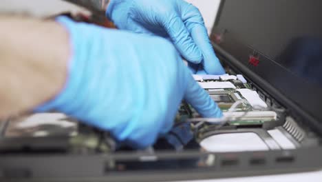una vista estática del técnico que trabaja está arreglando una computadora portátil vieja con guantes protectores e instalando piezas nuevas