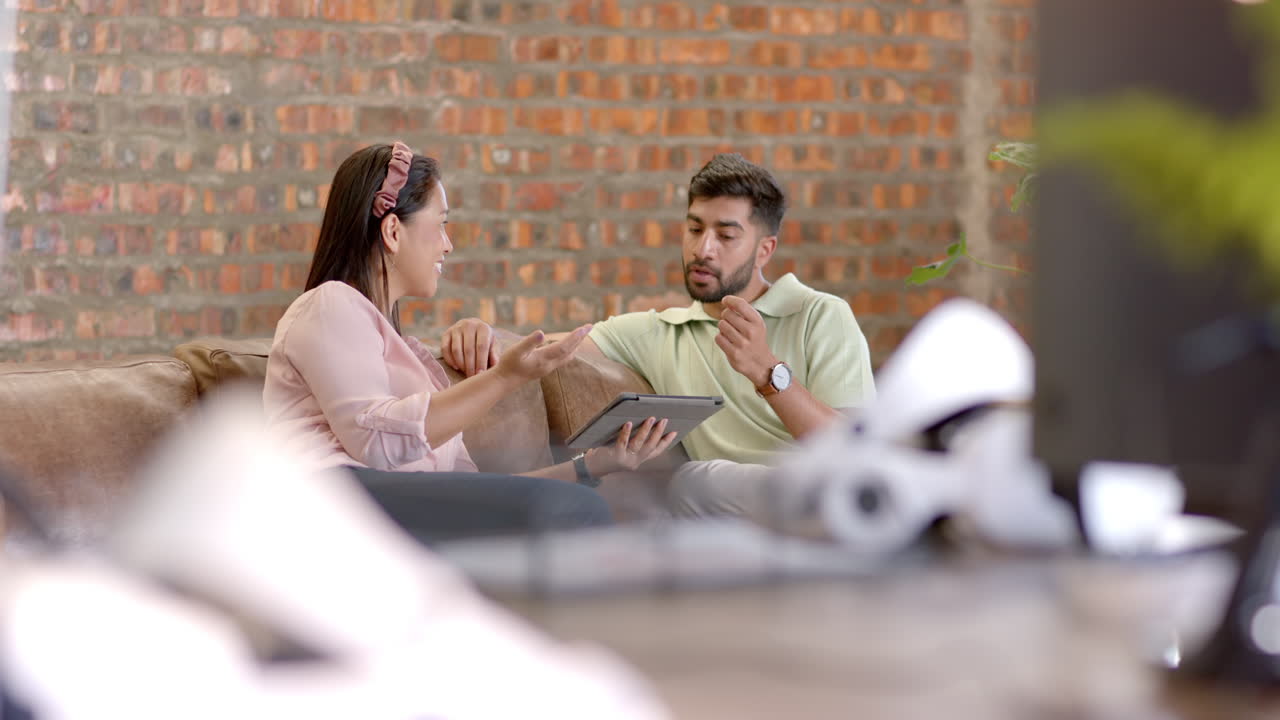 Discussing project details, colleagues using tablet while sitting on office couch