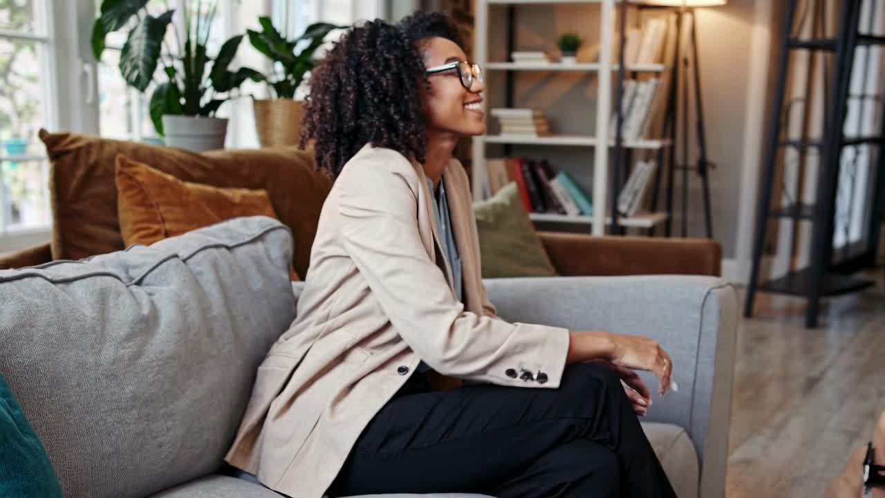 Side angle video of a woman in a beige blazer sitting on a cozy sofa in a modern living room