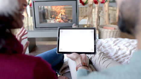 Pareja-Birracial-Con-Sombreros-De-Santa-Claus-Usando-Tableta-Con-Espacio-Para-Copiar-En-La-Pantalla-En-Casa,-Cámara-Lenta