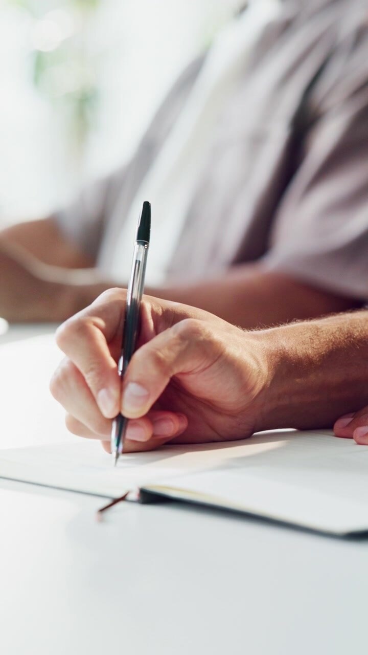 Primo piano di una persona che scrive su un quaderno a una scrivania