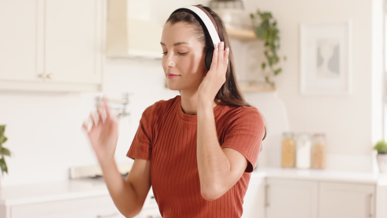 Woman in kitchen dancing joyfully while listening to music on headphones