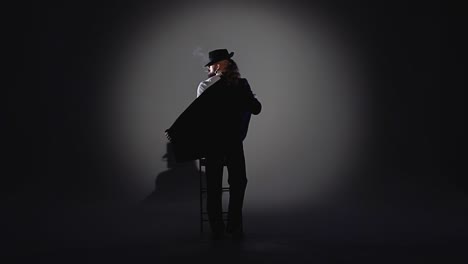 person in a hat stands in a dramatic spotlight