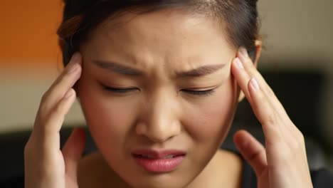 a woman sits at her desk in an office, rubbing her temples in frustration. it's a hectic afternoon, and she struggles to deal with mounting pressure from her workload.