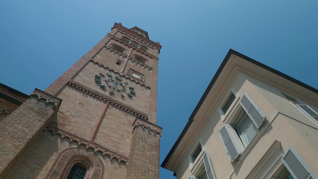 Campanile in mattoni, cattedrale, monumento storico con un orologio antico, vista dal basso sotto un cielo azzurro e limpido. Panoramica a mano libera che guarda in alto verso l'architettura medievale e le persiane tradizionali.