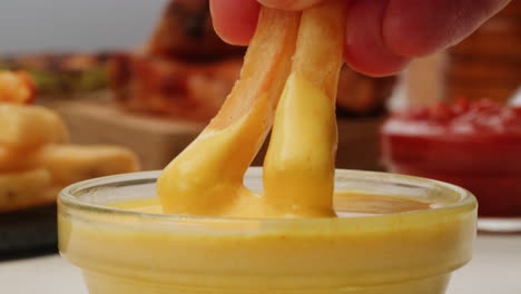 hand dipping french fries into mustard sauce