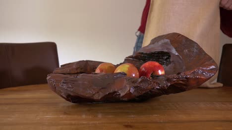 las manos masculinas toman frutas de una bolsa y las ponen en un tazón de madera sobre una mesa de madera, con una toma panorámica