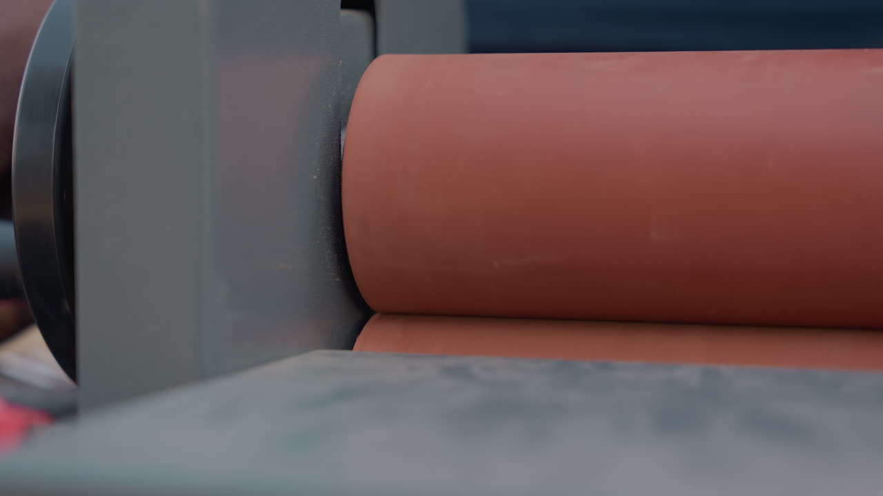Primo piano di un tamburo levigatore in officina, che mostra una mano che regola il rullo su una levigatrice pesante, con polvere sottile che si deposita su una tavola di legno usurata, catturando il processo di finitura meticoloso della falegnameria e l'abilità artigianale.