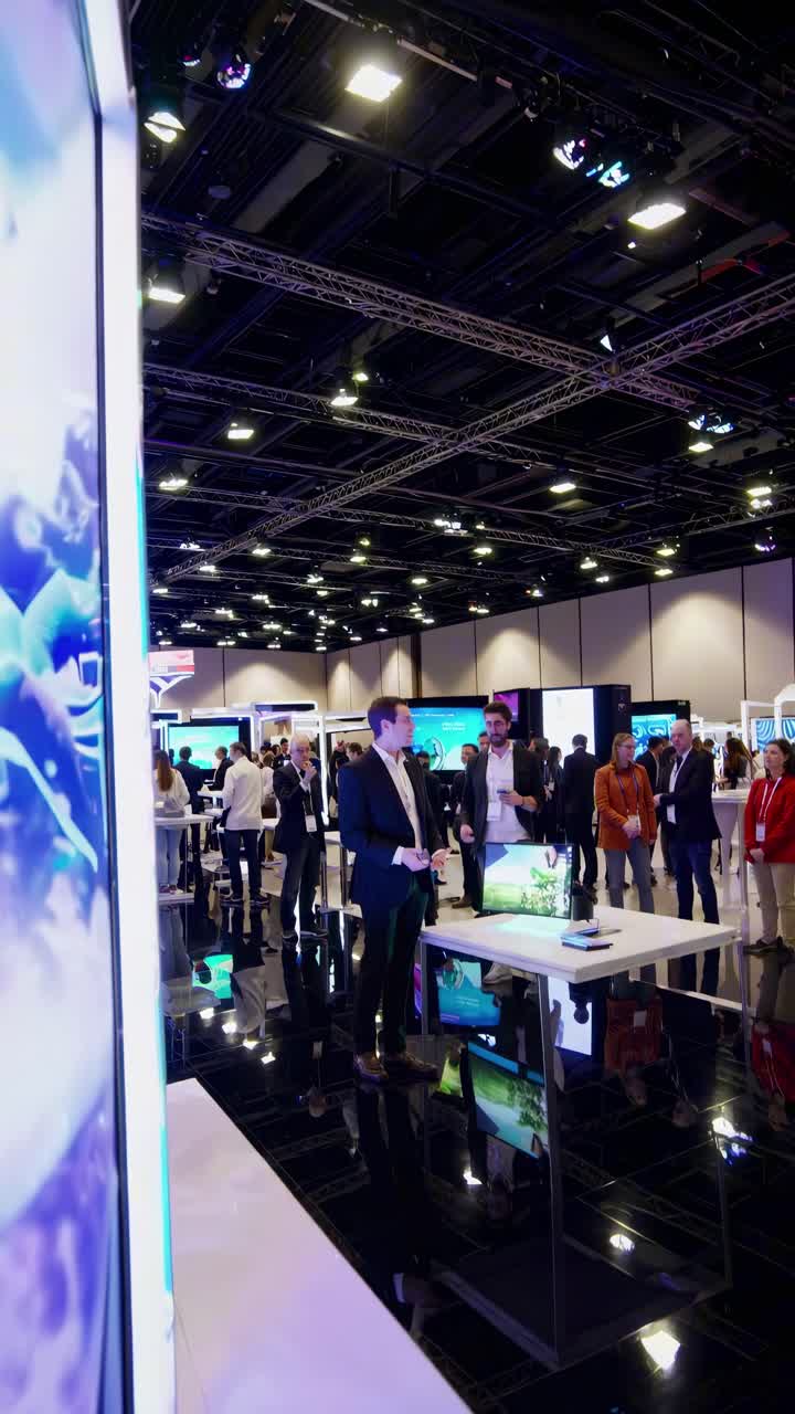 Scatto grandangolare di un'esposizione tecnologica con stand eleganti e schermi video, che cattura un'atmosfera vivace