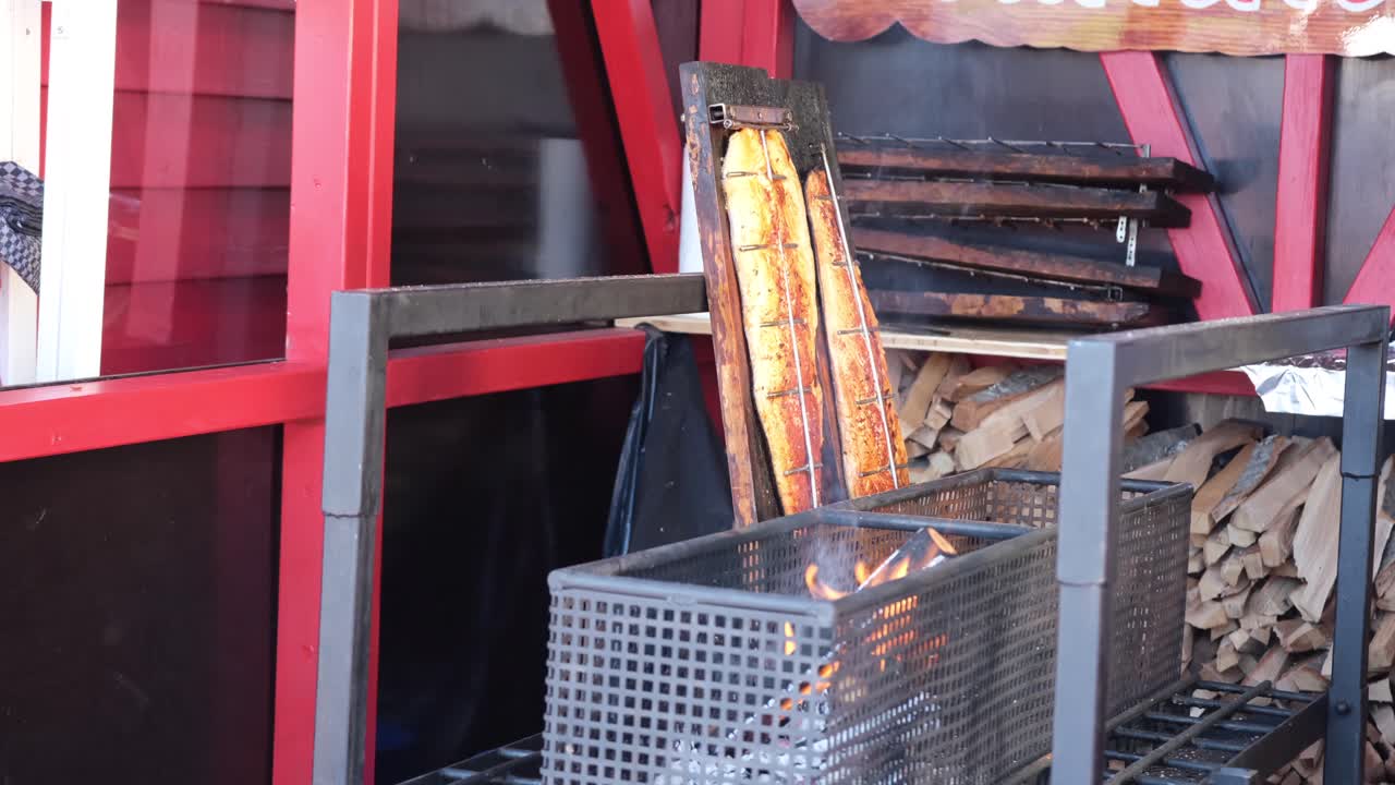 A close-up of a large salmon fillet slowly cooking over a wooden fire, with smoke infusing the fish, creating a rich, smoky flavor.