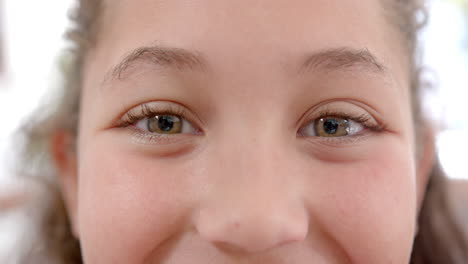ojos de una feliz chica biracial con el cabello largo y rizado de pie y sonriendo en la cocina soleada
