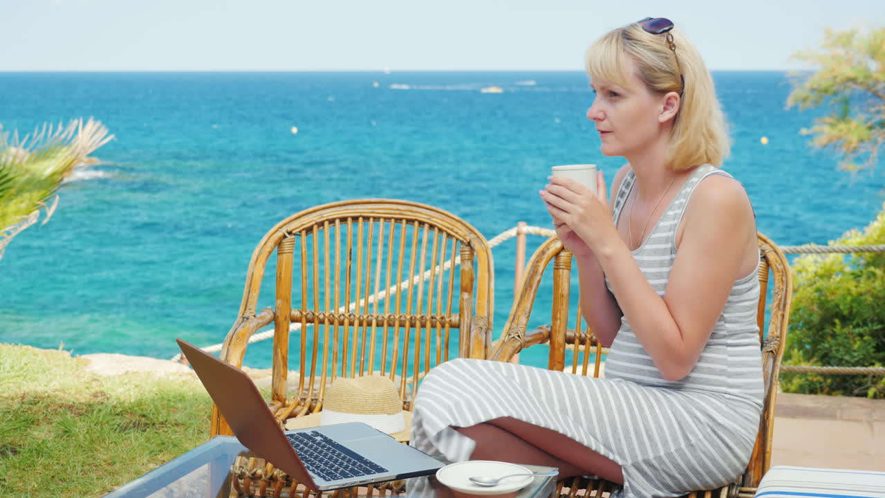 junge frau trinkt kaffee auf der terrasse mit blick auf das meer neben dem laptop perfekt fr