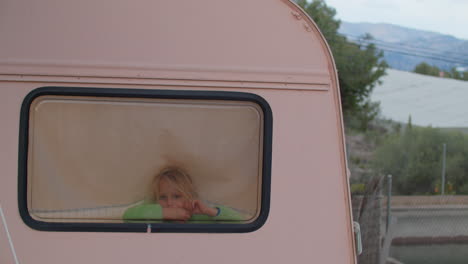 little blonde girl peeking out of camper van window