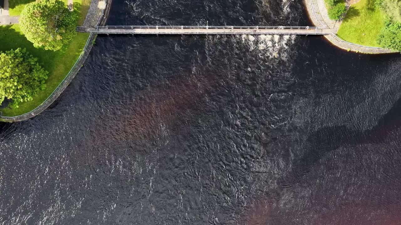 Drone captures hydroelectric dam, flowing river, and green landscape in bright daylight, smooth downward movement