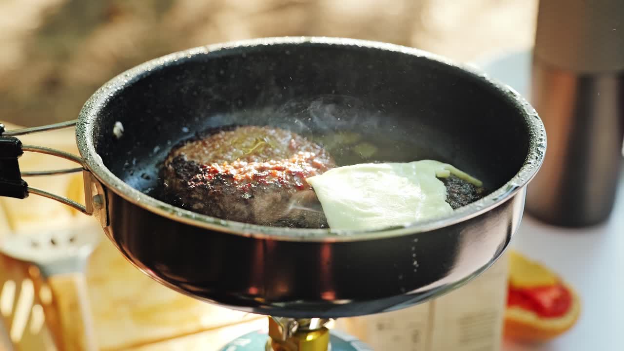 Slow motion hand places cheese on meat patties as smoke rises from hot pan