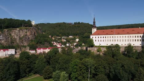 decin castle seen from a distance as the drone zooms in through soft fog at sunrise, with forest and city visible in czech republic