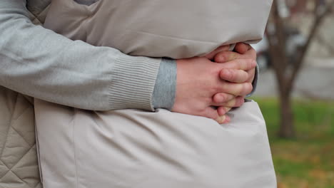 close up partial view of two people embracing in matching outfits, hands clasped tightly around waist, displaying warmth and intimacy in outdoor setting with blurred car visible in soft background