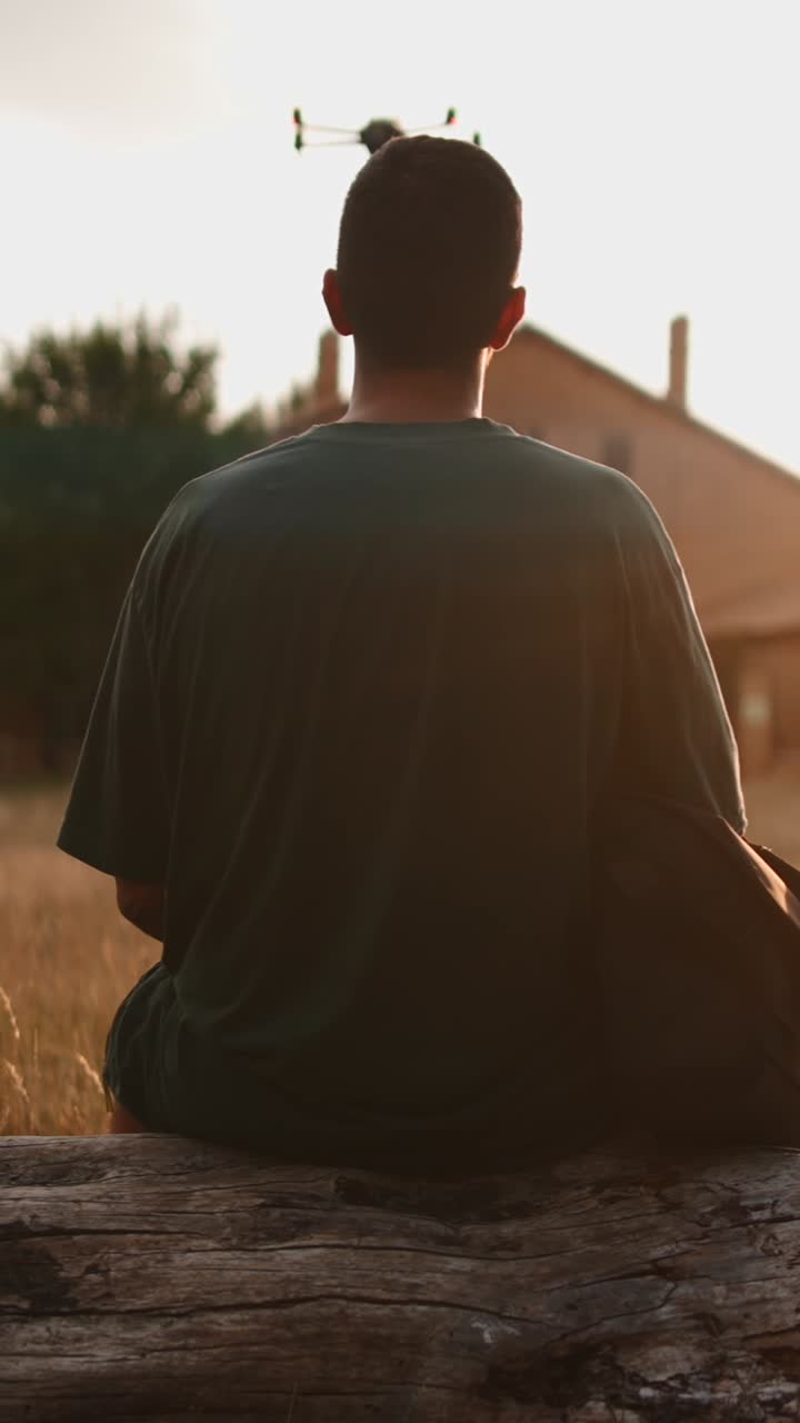 Person sitting on a log looking at a drone