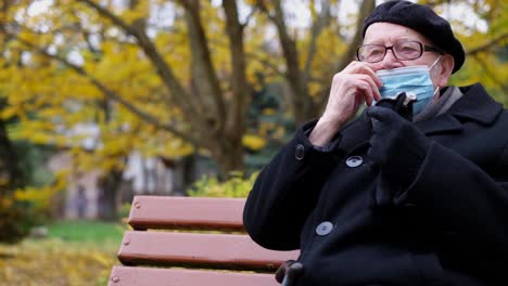 grandpa wears a protective blue mask while sitting on a park bench. threat of influenza virus infection.
