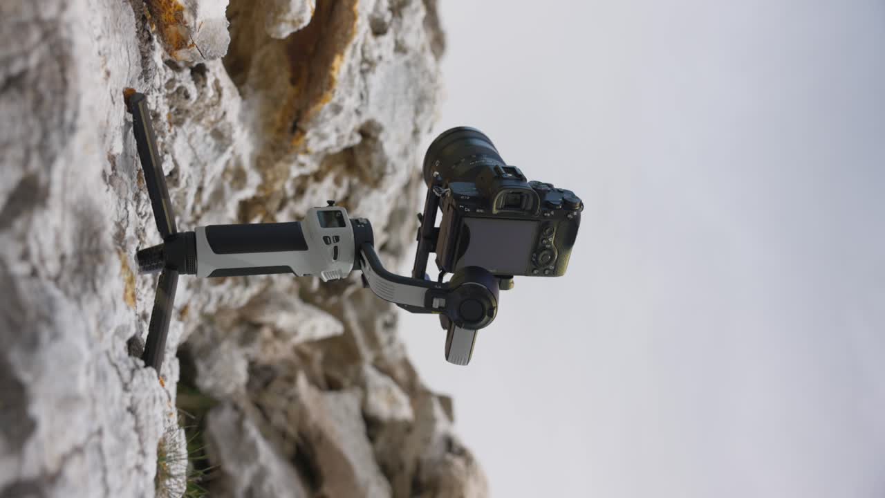 close-up de uma câmera montada em um gimbal portátil ligado a uma superfície rochosa, mostrando a tecnologia de estabilização em ambientes acidentados