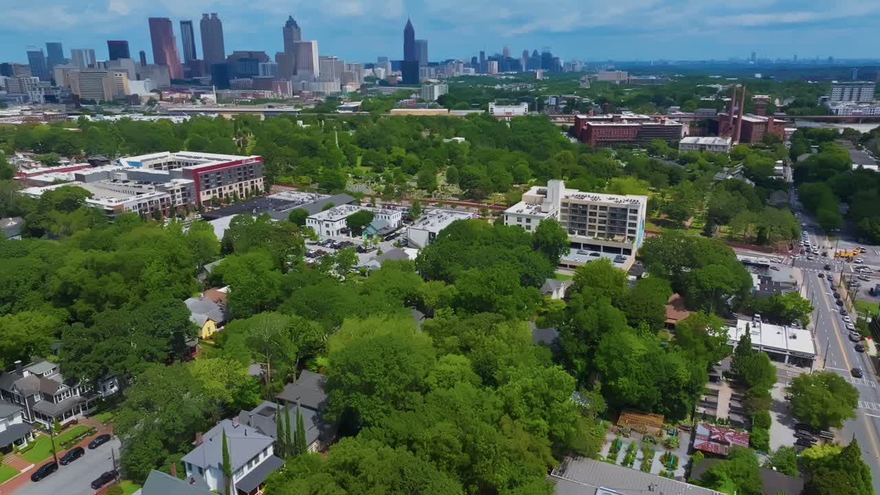 Drone flight over idyllic suburb neighborhood with apartments and parking cars in Atlanta. Skyline with high-rise towers and buildings in background. Sunny summer day with green trees. Aerial flyover