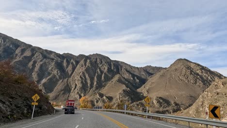 a vehicle travels through queenstown's mountainous landscape in autumn, showcasing vibrant foliage and rugged terrain under clear skies