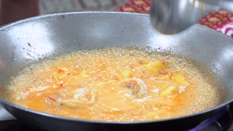 close up view of a chef using a steel wok to prepare a thai red curry dish with fresh prawns and pineapples