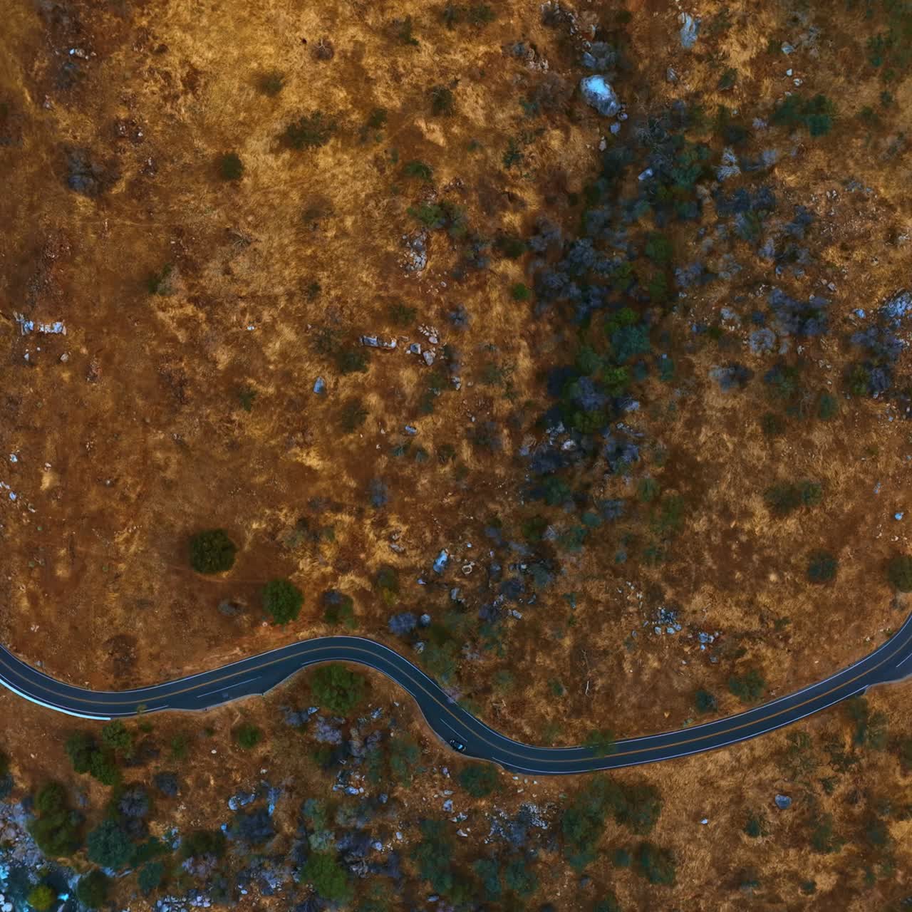 Wavy highway in the rocks. Lonely red car runs by the road. Mountain river floats near the highway. Top view