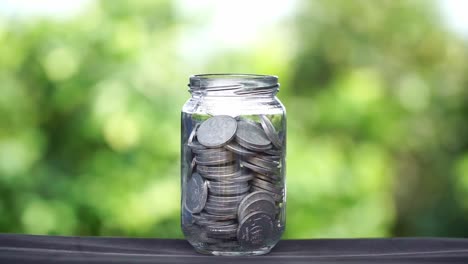 coins falling into a glass with blur green nature background. business concept, profit and saving.