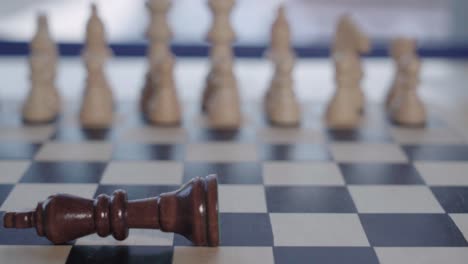 king chess piece falls over in front of soft focus white army, closeup