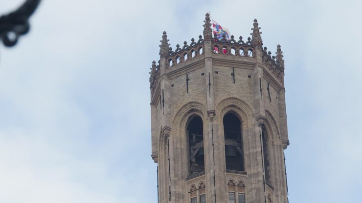 La panoramica della telecamera verso l'alto rivela il campanile medievale, l'orologio e i fiori rosa sotto il cielo diurno