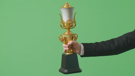 close up of business man's hand holding a gold trophy to his side showing award winning as the first winner on green screen background in the studio