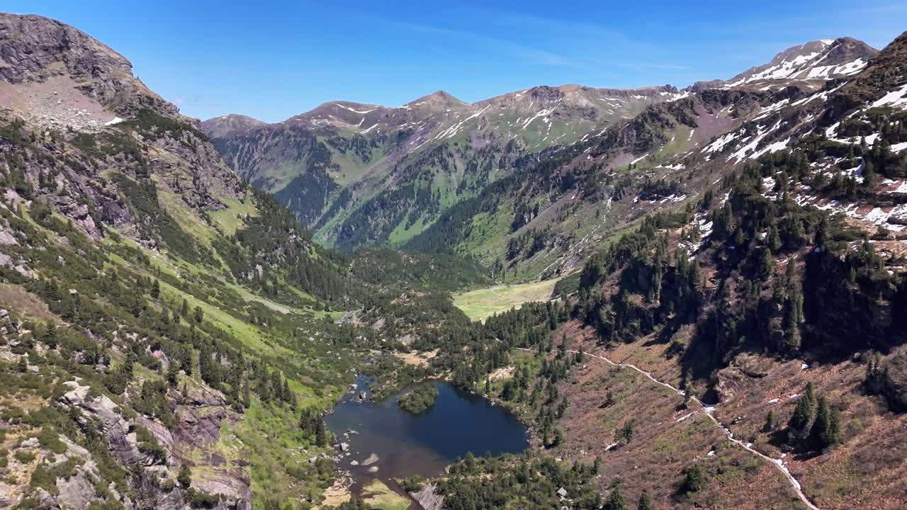 Alpine valley in Murgsee, Switzerland featuring steep green slopes, dense forests, cliffs, and scattered snow on high peaks beneath a vivid blue sky, creating a striking natural mountain landscape