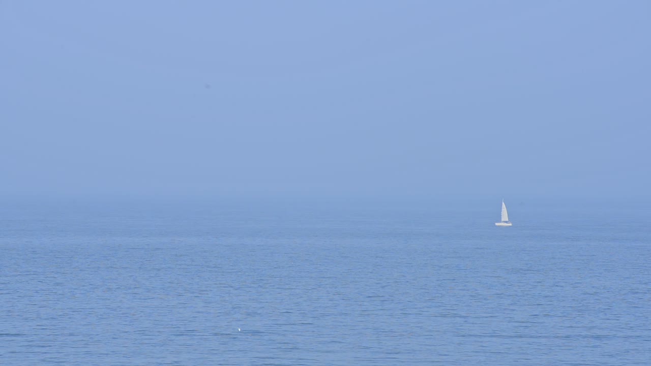 A white sailboat sailing on the blue waves of England - wide shot